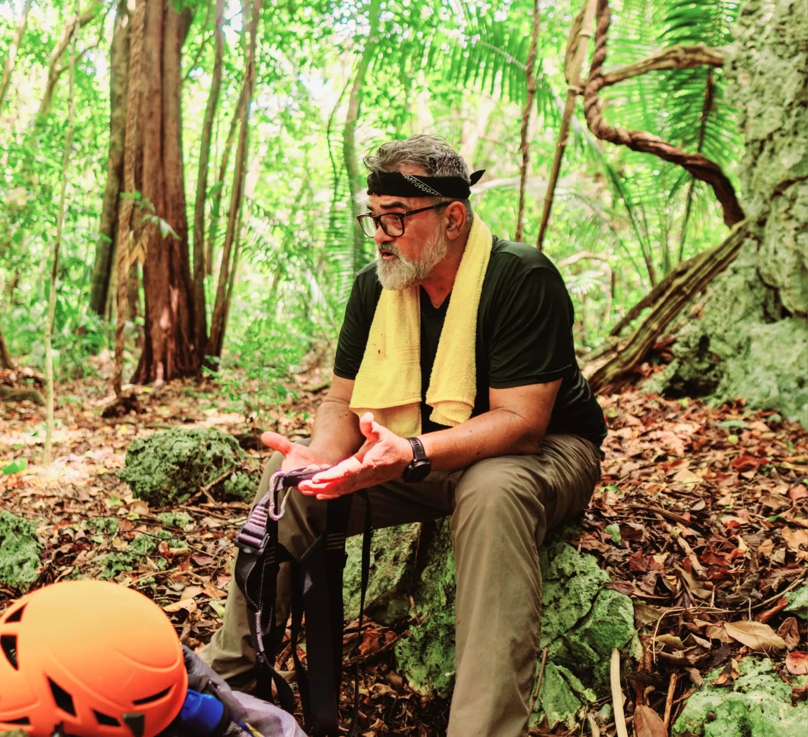 Matthew Harper seated among trees and rocks, talking with visitors on a forest trail